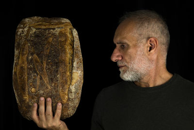 Close-up portrait of a man holding whole bread against black background