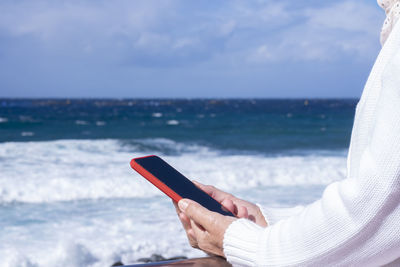 Man using mobile phone in sea against sky