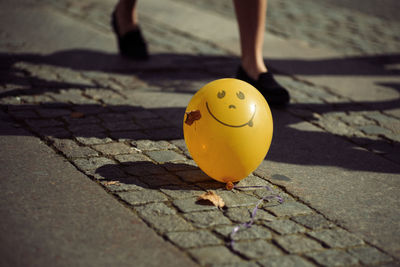 Low section of person walking by yellow balloon on footpath 