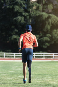 Rear view of athlete with prosthetic leg running on field