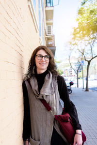 Smiling woman with eyeglasses leaning on wall, looking away