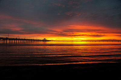 Golden waves lit up by a orange sunrise over a pier