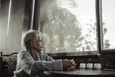 Young woman looking through window at home