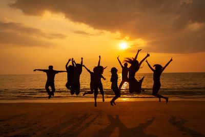 Silhouette people jumping at beach against sky during sunset