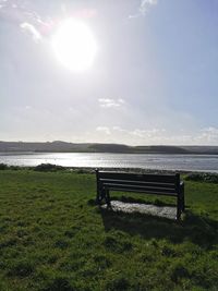 Bench on field by sea against sky