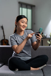 Young woman using mobile phone while sitting on sofa at home