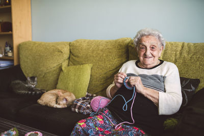 Portrait of crocheting senior woman sitting on couch besides her sleeping cats