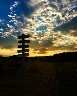 Silhouette cross on field against sky during sunset