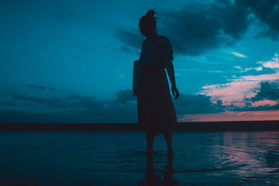 Silhouette woman standing by sea against sky at sunset