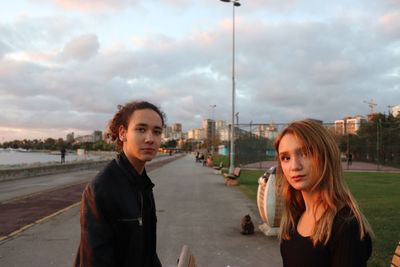 Portrait of friends standing on road in city against sky