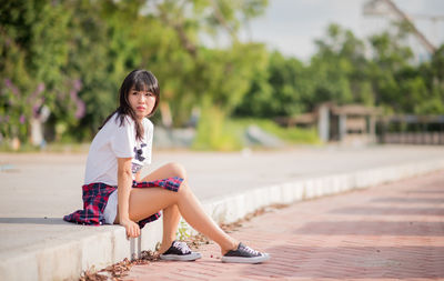 Portrait of young woman standing on tree trunk