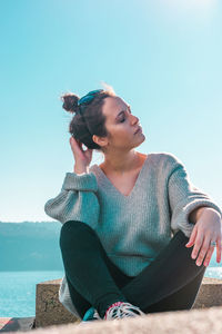 Young woman sitting on retaining wall against sea