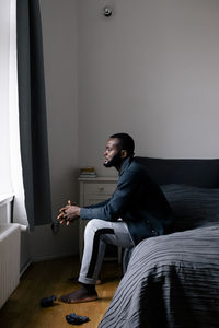 Full length side view of thoughtful man sitting on bed at home