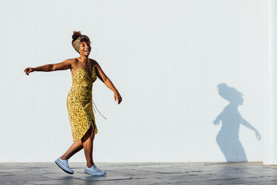 Side view of delighted black female in trendy clothes turning around on street while enjoying summer weekend and smiling