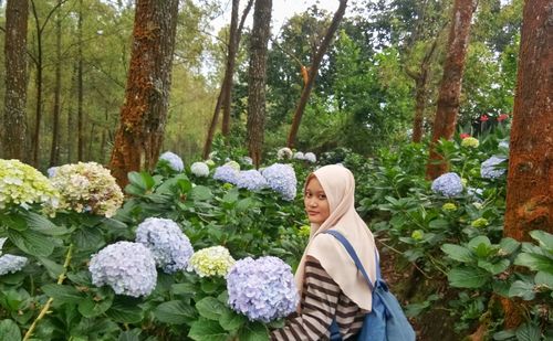 Portrait of woman standing by plants against trees