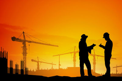 Silhouette people working on construction site against orange sky