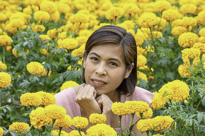 Portrait of smiling woman sitting against yellow flowers