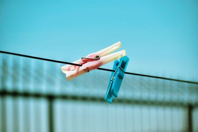 Low angle view of clothespins on clothesline against clear blue sky