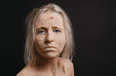 Portrait of woman with muddy face over black background
