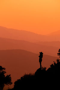 Rear view of man standing on mountain against sky during sunset