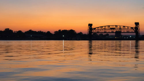 Silhouette bridge over river against sky during sunset