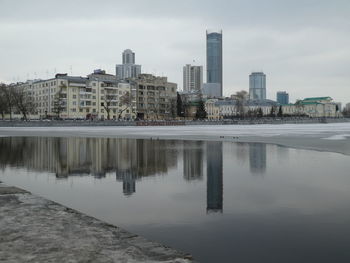 Reflection of buildings in lake against sky in city