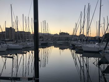 Sailboats moored in harbor at sunset