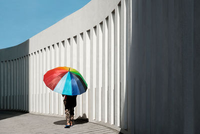 Rear view of a boy with umbrella walking against white column building