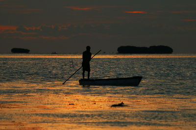 Silhouette man rowing boat on sea during sunset