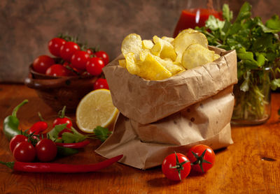 Close-up of potato chips by tomatoes in paper bag on table