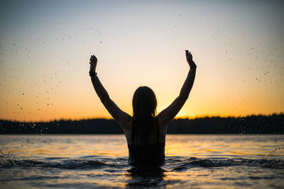 Beautiful girl in a long black swimsuit swims on the lake in the rays of sunset or dawn