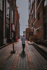 Rear view of man walking on cobblestone street in city