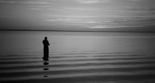 Silhouette man standing at sea shore against sky