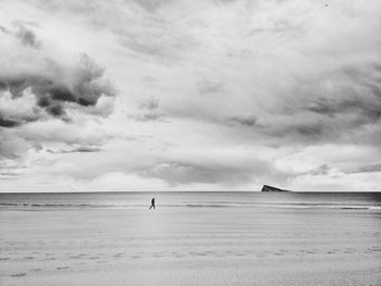 Lonely man walking at beach against cloudy sky