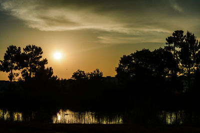 Silhouette trees by lake against sky during sunset