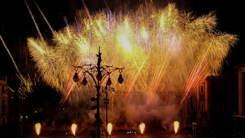 Street light against firework display in sky at night