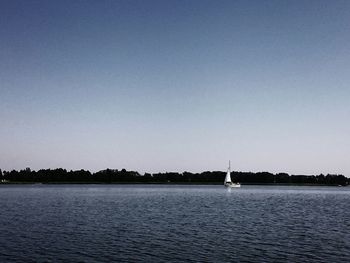 Boats in calm sea against clear sky