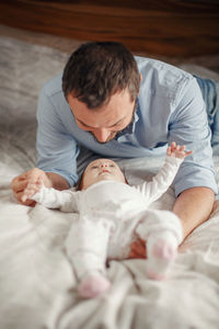 Cheerful father playing with daughter while lying on bed at home