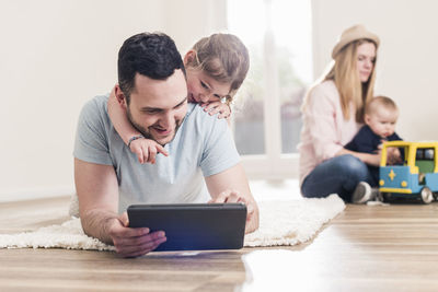 Father and daughter using tablet in new home with woman and baby in background