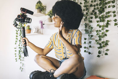 Young afro influencer waving while vlogging through camera at home