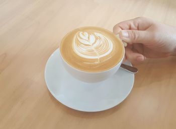 Human hand carries a cup of hot latte coffee with art design foam on top
