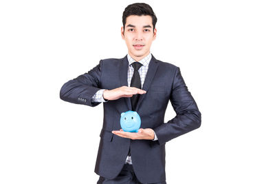 Portrait of businessman with piggy bank standing against white background