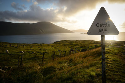 Road sign on field against sky during sunset