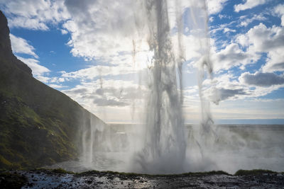 Close-up of seljalandsfoss with mist flowing from mountain against blue sky