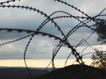 Close-up of barbed wire fence against sky