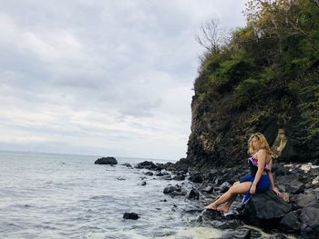 Side view of woman sitting on rock at seashore