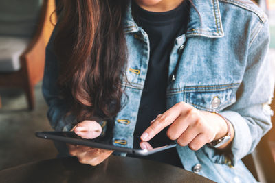 Midsection of woman using digital tablet while sitting at cafe table