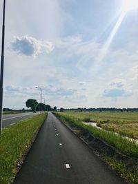 Empty road amidst field against sky