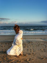 Rear view of woman on beach against sky