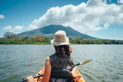 Rear view of woman sitting in boat on lake against sky